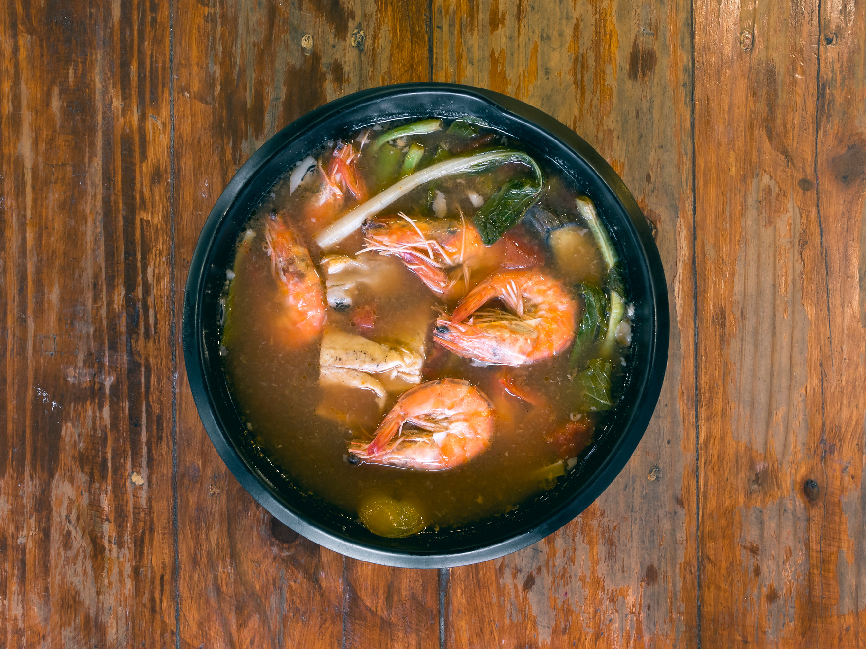 Sinigang na Hipon is a type of Filipino sour tamarind soup. Top view, on a wood table.